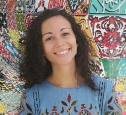 Smiling woman with curly hair in front of a brightly colored mural. 